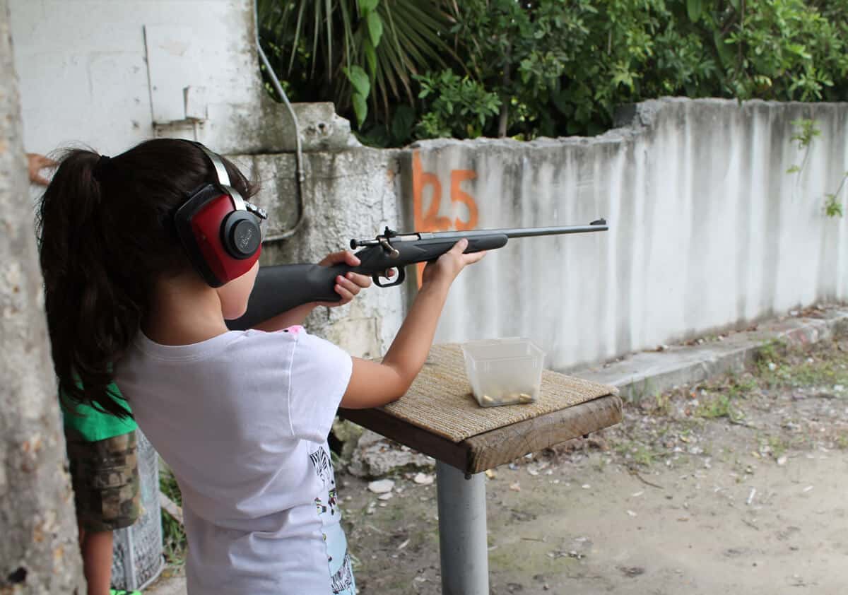 Child with ponytail taking aim with a rifle