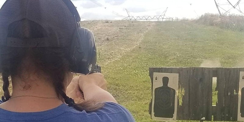 person in braids aiming a gun at a target